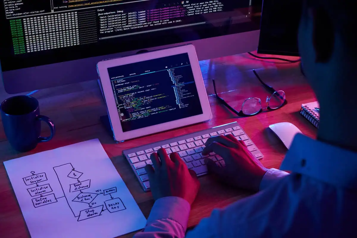 Programista kodujący na tablecie i komputerze stacjonarnym z diagramem przepływu i środowiskiem programistycznym.