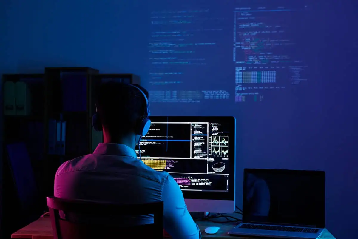 Programista w słuchawkach pracuje przy monitorach z kodem, kod wyświetlony na ścianie.