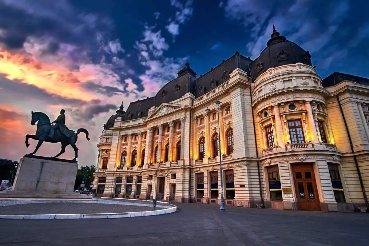 The Central University Library of Bucharest, Romania, glowing under the evening sky, accompanied by the statue of King Carol I.