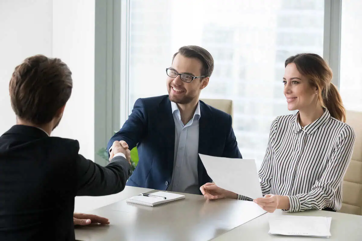 Three business professionals shaking hands across a meeting table.