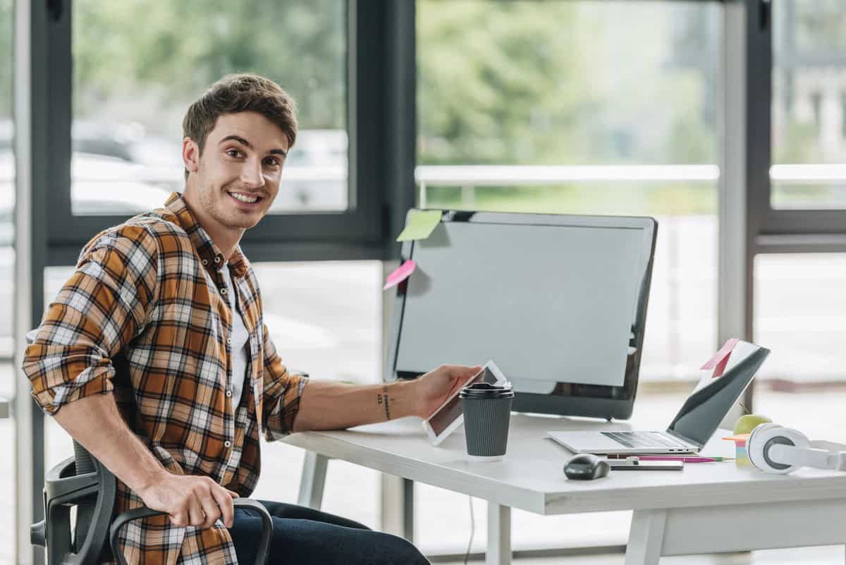 Graphic designer with tattoos working at a desk with a digital tablet and computer. testimonial