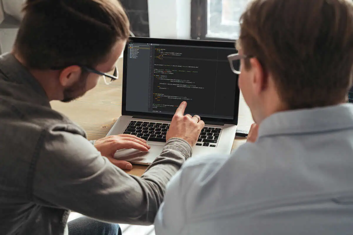 Two developers collaborating, looking at code on a laptop screen.