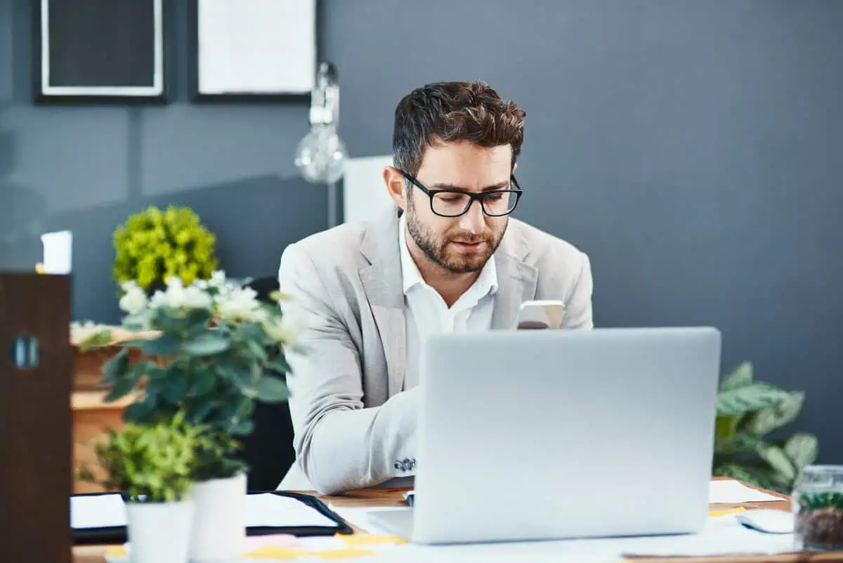 Two male developers sitting side-by-side, working on laptops in a modern office.