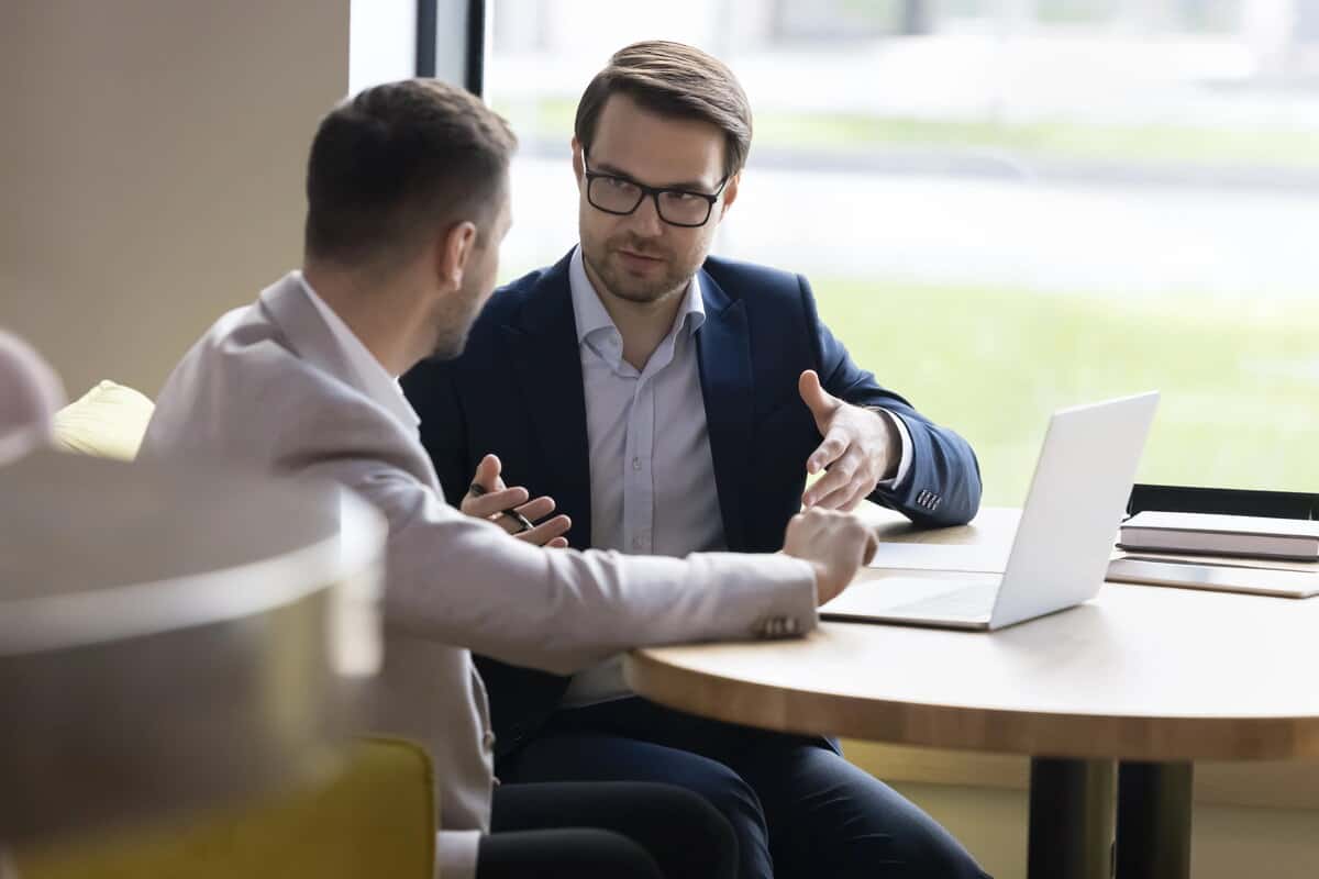 Two professional men in suits talking over a laptop at a round table. testimonial