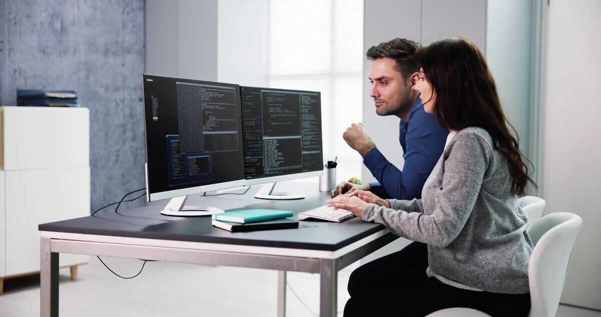 Two data scientists working together on code and analytics displayed across dual monitors in a modern office testimonial