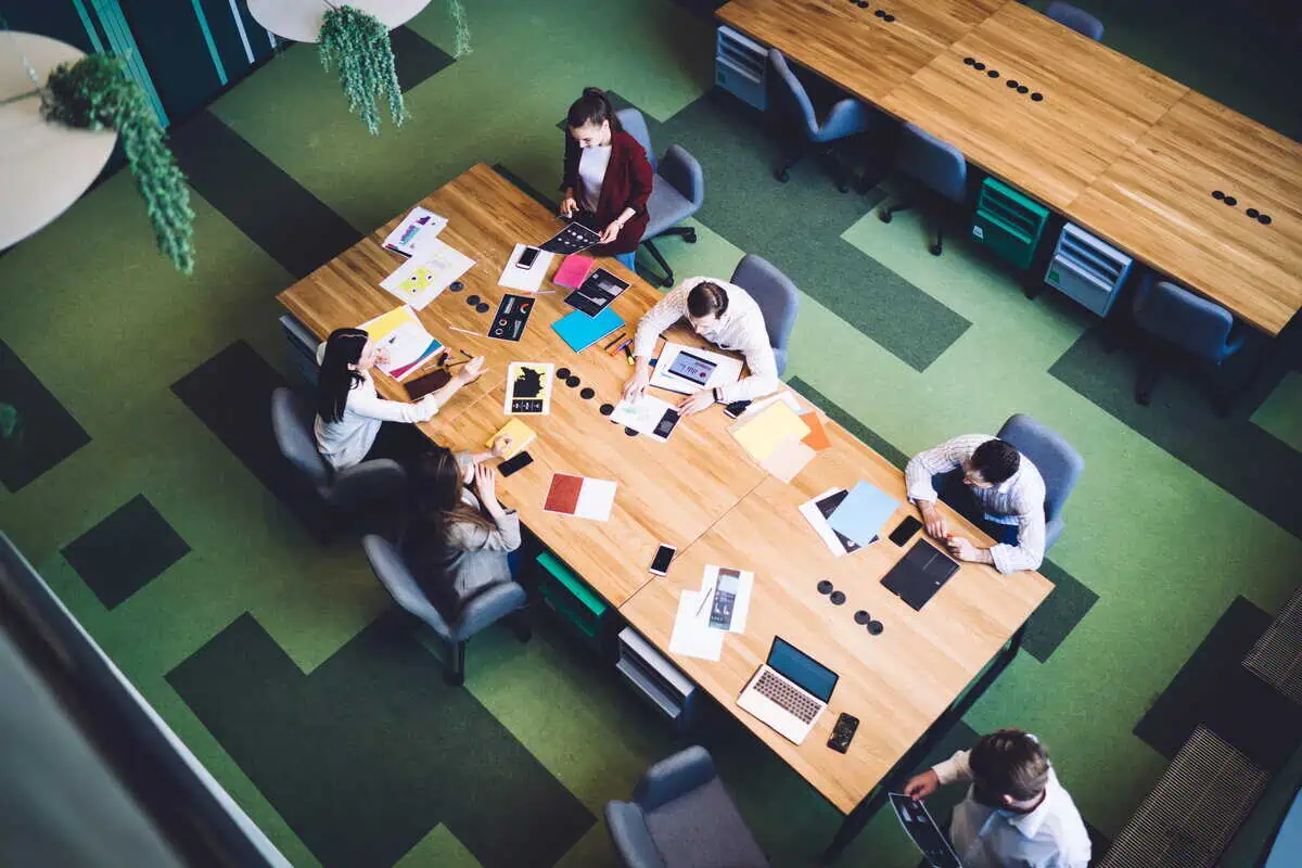 An overhead view of a diverse team of professionals collaborating around a large wooden conference table in a modern office space.